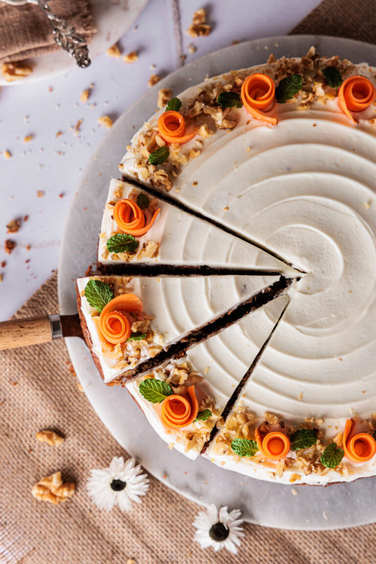 Karottenkuchen mit Frischkäse Topping, hübsch dekoriert it Möhrenröschen, gehackten Walnüssen und Minzblättern